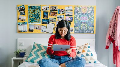 Student sat on the bed and using a tablet in the accommodation