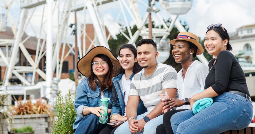 A group of five students on a bench with a ferris-wheel in the background