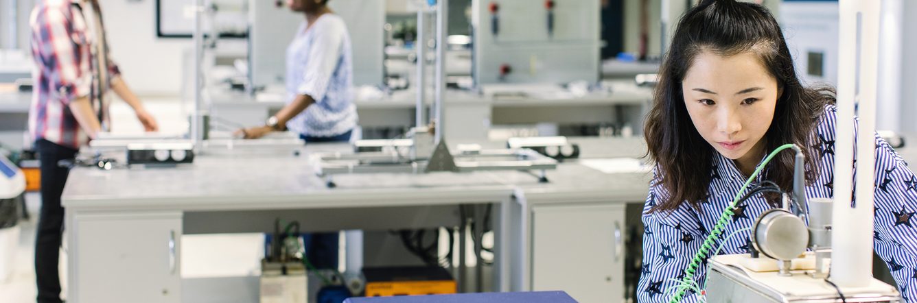 A student studying at the lab and two students are talking behind her