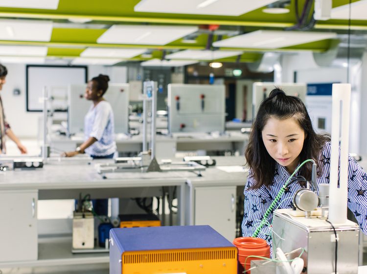 A student studying at the lab and two students are talking behind her