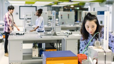 A student studying at the lab and two students are talking behind her