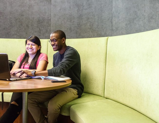 Two students smiling and looking at a laptop