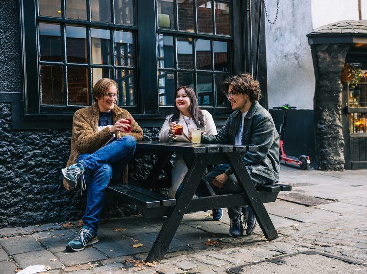 students sitting on a bench, having beverages and enjoying the weather outside