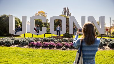 A student in front of the UCONN sign at the university campus