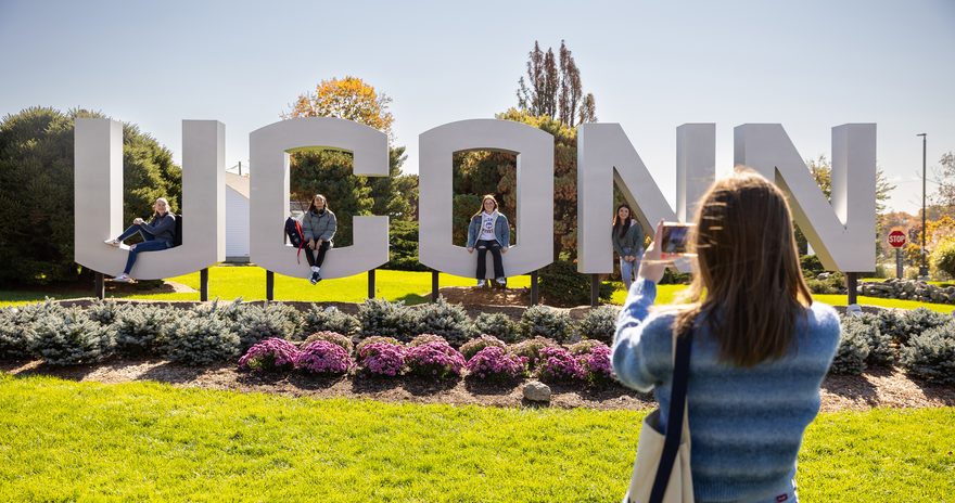 A student in front of the UCONN sign at the university campus