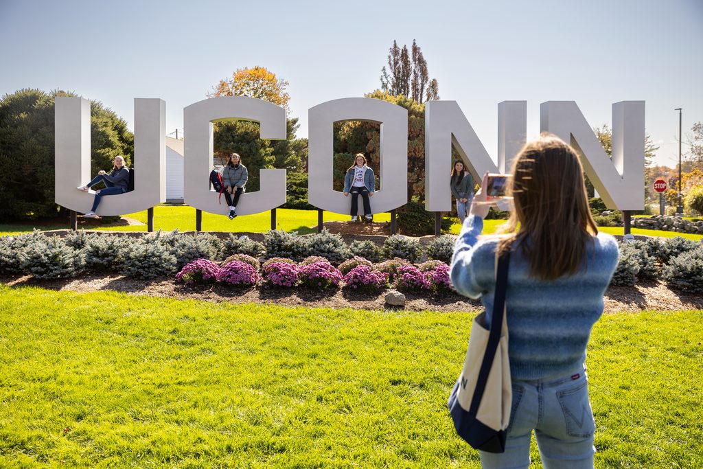 A student in front of the UCONN sign at the university campus