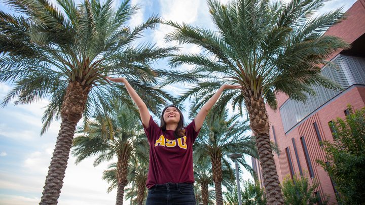 Student raising her arms to the sky and smiling under palm trees