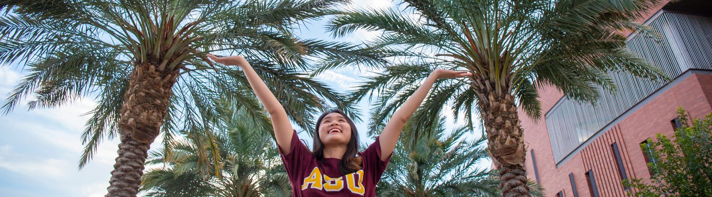 Student raising her arms to the sky and smiling under palm trees