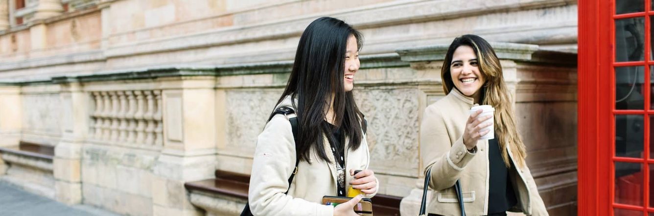 Two students walk through London talking and laughing