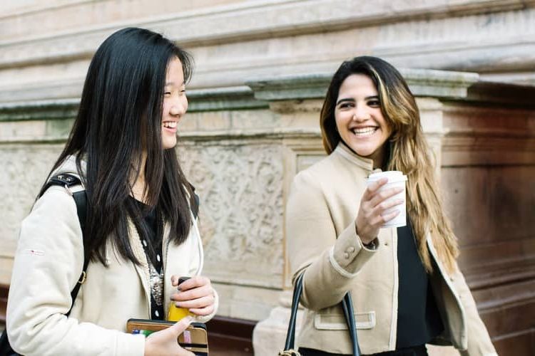 Two students walk through London talking and laughing