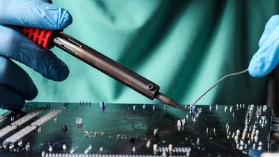 student learning electronic circuit board with soldering iron at table