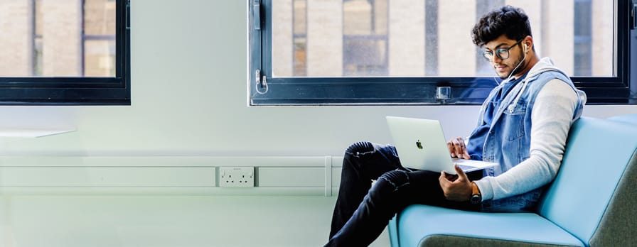 A young man sits alone with a laptop and headphones