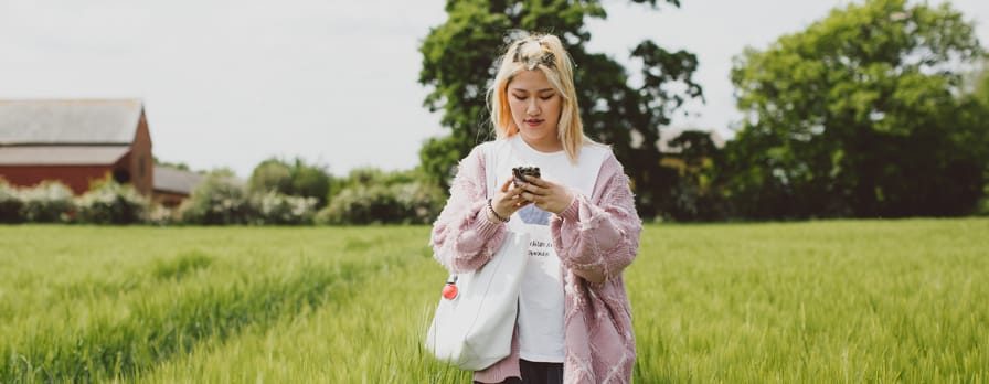 A young woman walks through a field while looking at her phone