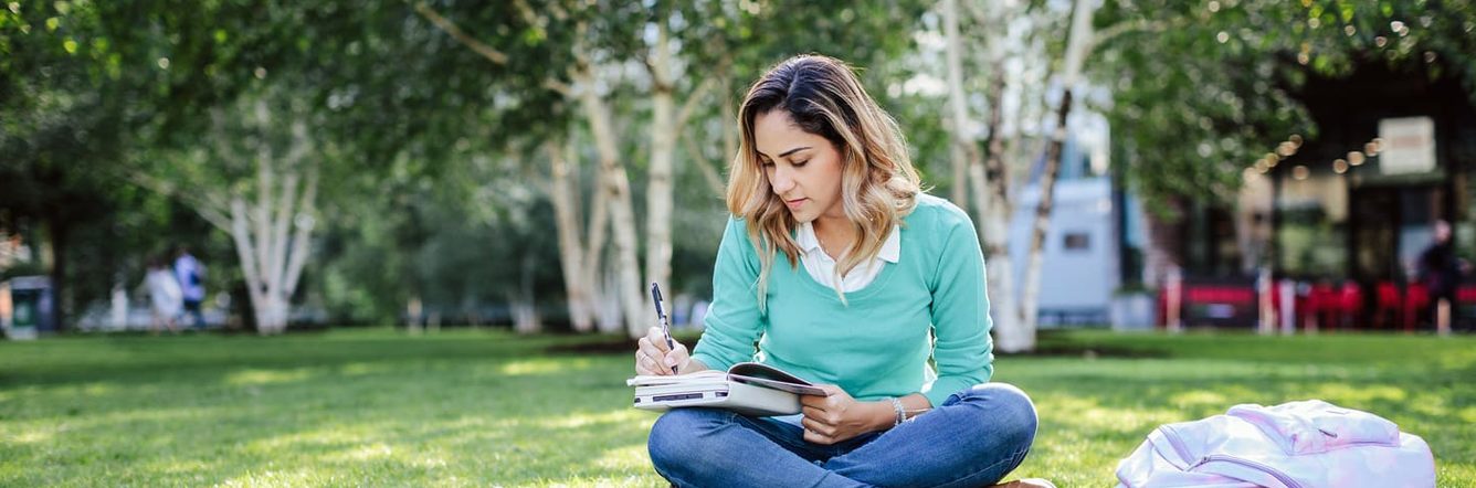 student writing in her book in the park