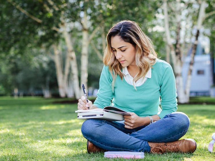 student writing in her book in the park