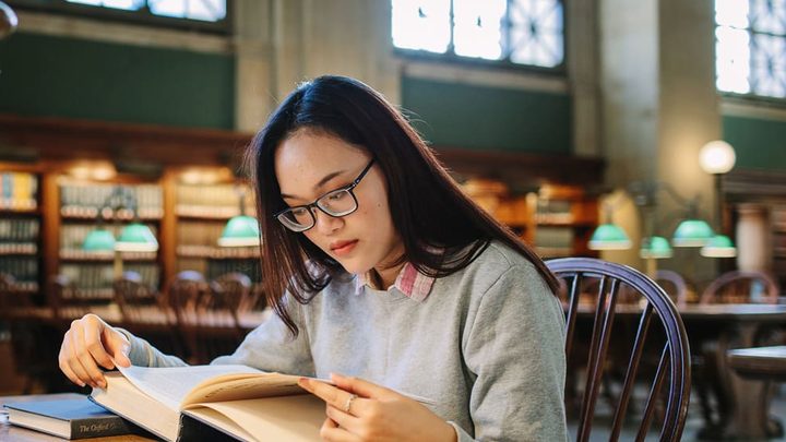 female student reading book in library