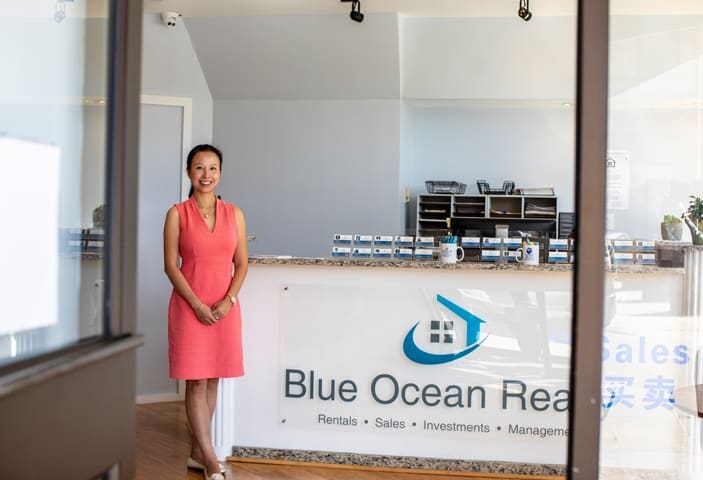 OPT: A woman in a coral dress standing smiling outside a realty office