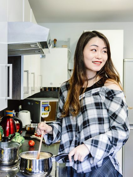 A student in a checkered shirt cooking in a shared kitchen.
