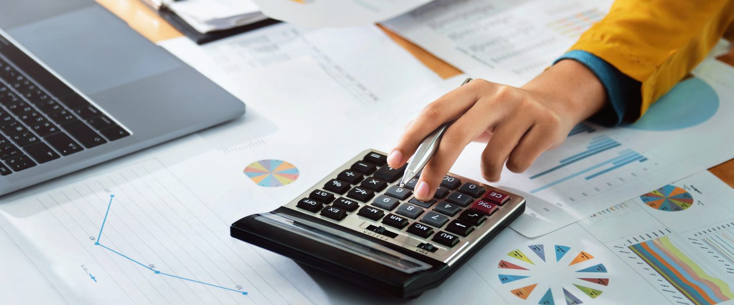 A woman's hand using the calculator and taking in information from graph's