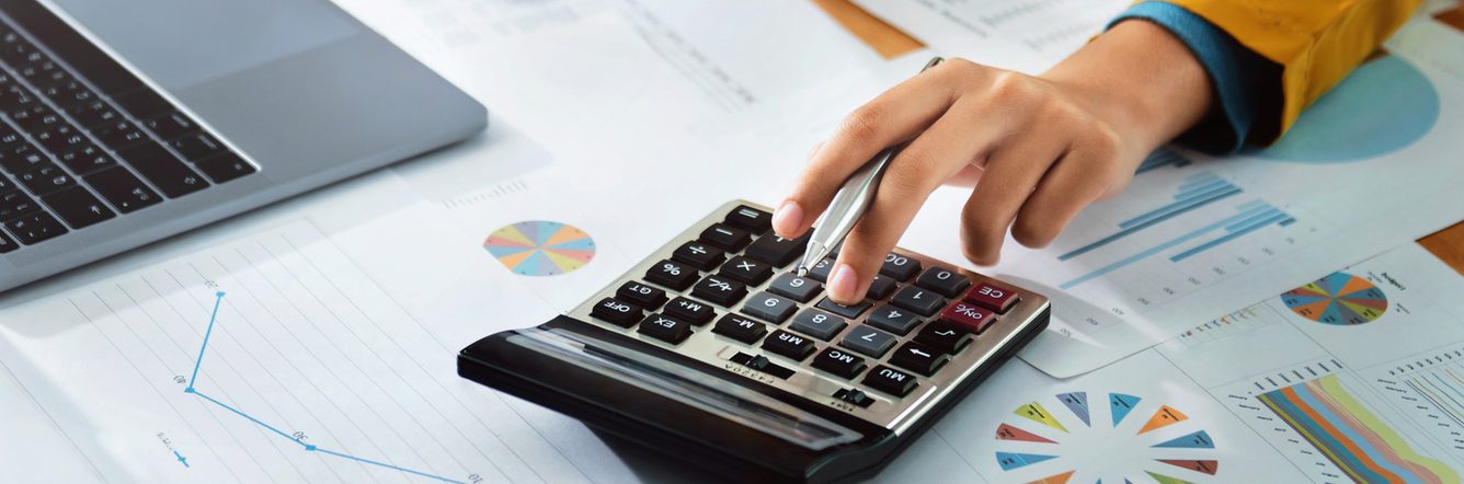 A woman's hand using the calculator and taking in information from graph's