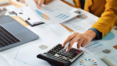 A woman's hand using the calculator and taking in information from graph's