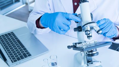 A person in a lab coat looking at a microscope.