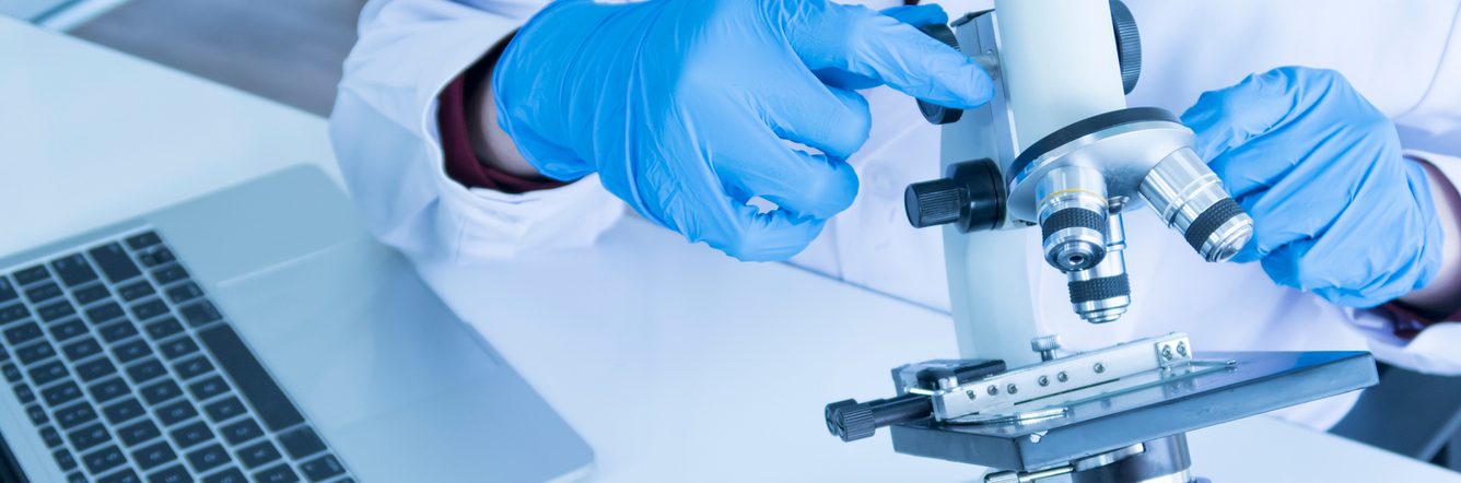 A person in a lab coat looking at a microscope.