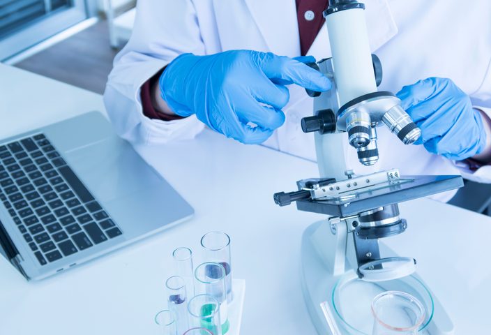 A person in a lab coat looking at a microscope.
