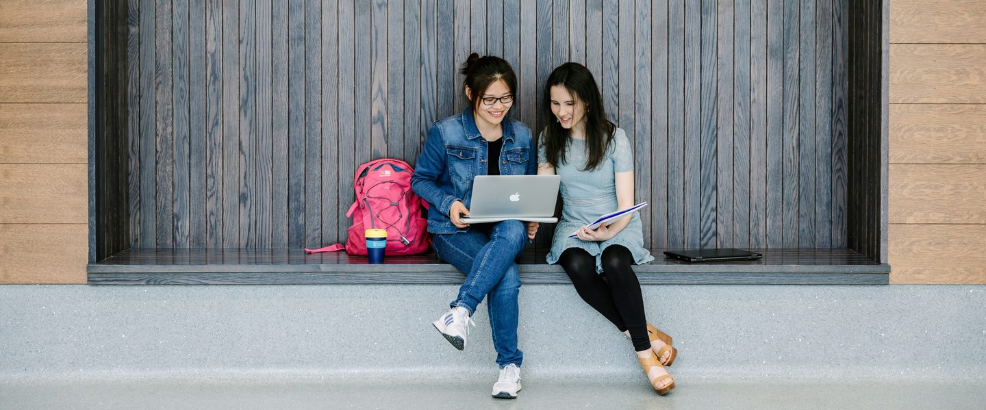 Two students looking at their laptop in a communal area