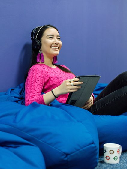 Girl sitting on a blue bean bag listening to a podcast