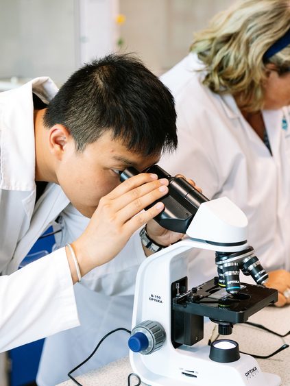 Two students doing practical work with microscopes alongside their lecturer.