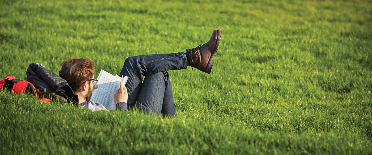 University of Birmingham students reading a book on campus grass