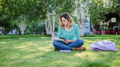 Student taking notes in her diary while sitting outdoors in the park
