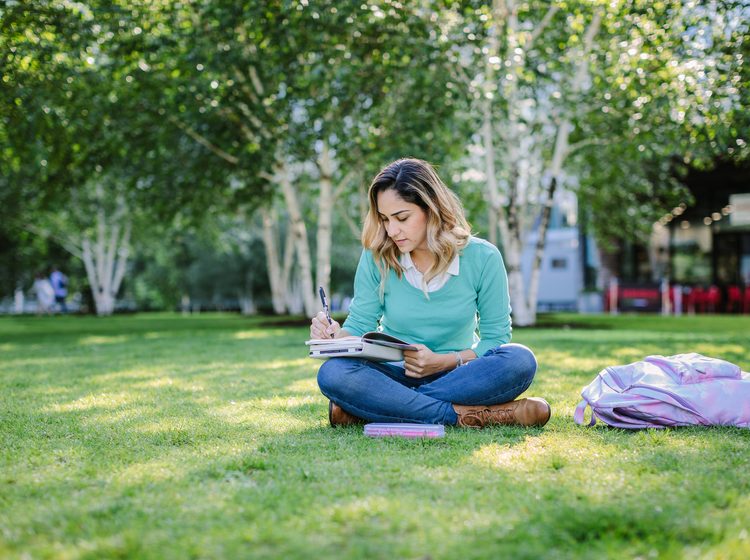 Student taking notes in her diary while sitting outdoors in the park