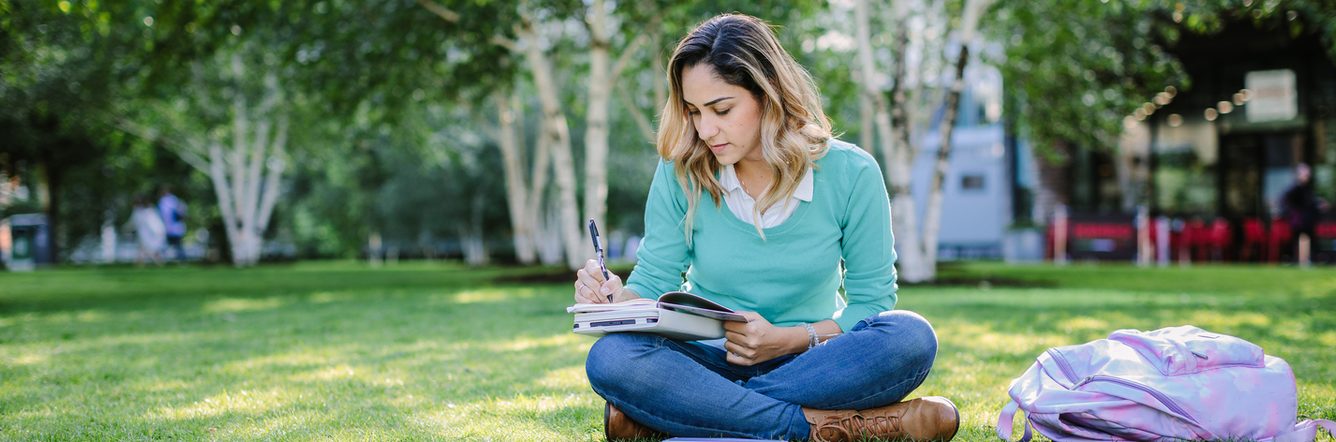 Student taking notes in her diary while sitting outdoors in the park
