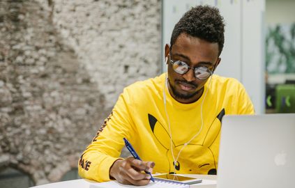 Student wearing a bright yellow t-shirt wearing earphones while revising lectures