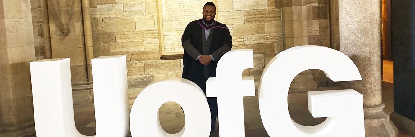 David posing with the University of Glasgow sign