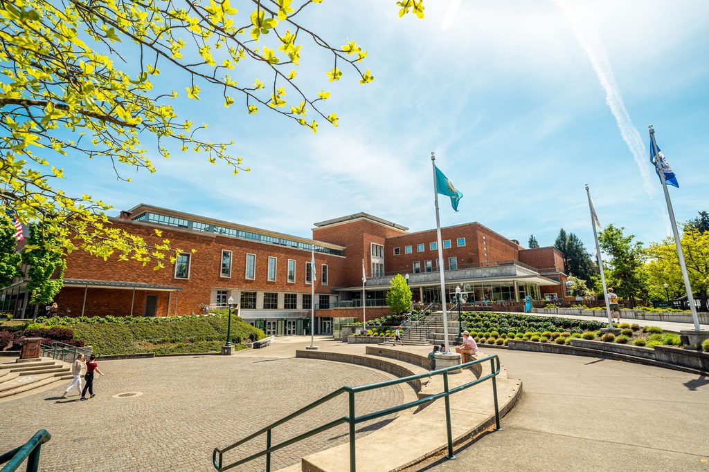 Students walking in front of the UO campus building on a clear sky day