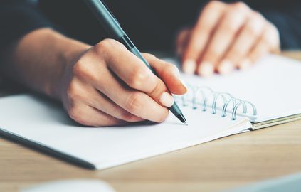 Close up of hands writing on a spiral notepad