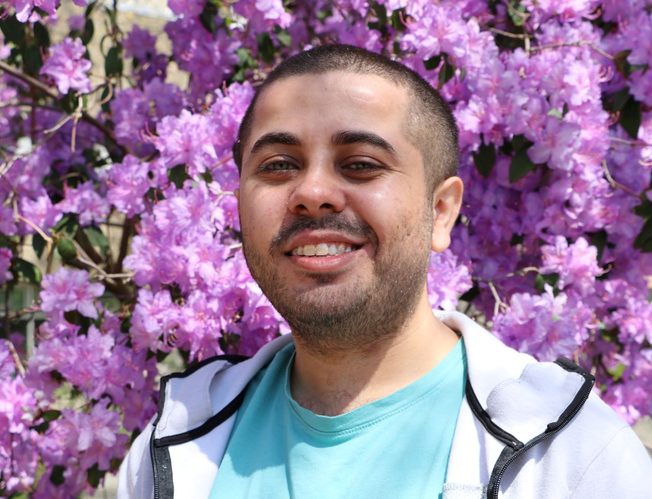 Ankit smiling in front of a tree with flowers
