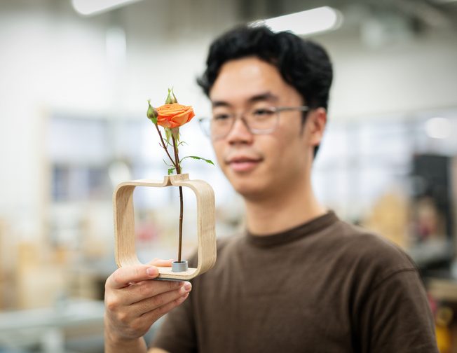 Student presenting a design project featuring a wooden vase and flower at ECU